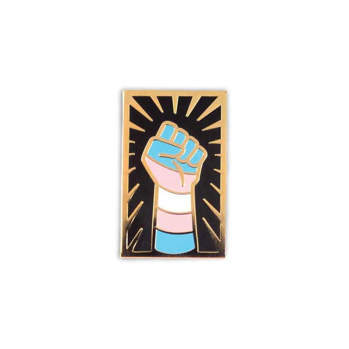 Enamel pin of a raised fist colored like the transgender flag with gold outlining against a black background with a gold sunburst.
