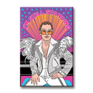 An illustration of Elton John in a white suit with feathers on the shoulders and oversized amber and bejeweled glasses in front of a black piano and purple background with blue stars with "I'M STILL STANDING" in pink around his head. 