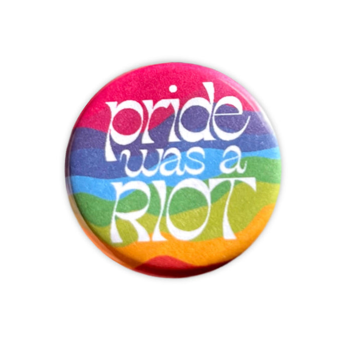 Round magnet with wavy rainbow colored horizontal stripes with large white lettering that says 