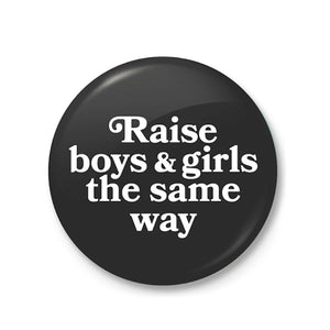 This larger, 2.5-inch button features a black background, white text saying “Raise Boys & Girls The Same Way”, and has a latch mechanism backing. 