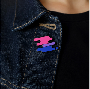 Enamel pin of a squiggle with the bisexual pride flag colors on the lapel of a denim jacket.