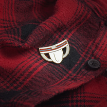 Load image into Gallery viewer, Enamel pin of a white jockstap with red and blue stripes across the band attached to a red and black buffalo check shirt. 