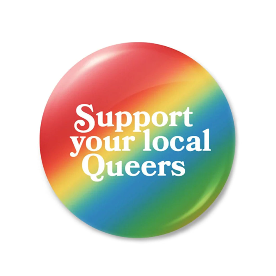 This larger, 2.5-inch button features a rainbow-ombre background, white text saying “Support your local Queers”, and has a latch mechanism backing. 