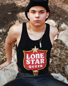 A picture of a model wearing the tank top with black pants and a beanie sitting on rocks. 