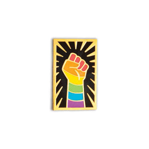 Enamel pin of a raised fist colored like the rainbow pride flag with gold outlining against a black background with a gold sunburst.